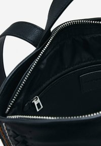 Czarna skórzana torebka z otwartym srebrnym suwakiem, ukazująca czarną tkaninową wyściółkę i wewnętrzną kieszeń na suwak.