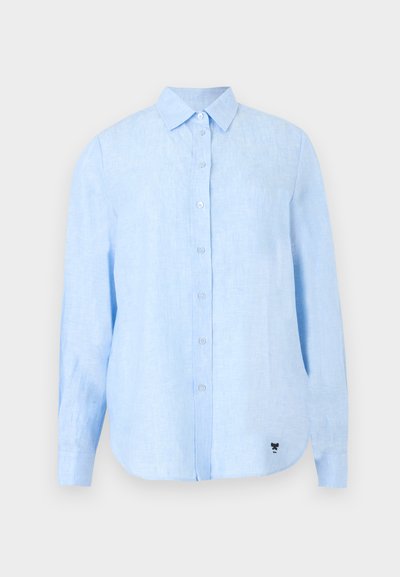 Chemise bleu clair à manches longues avec col, en tissu texturé, avec un petit logo noir près de l'ourlet inférieur.