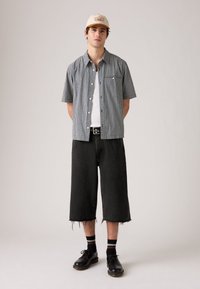 Kortermet, rutete skjorte i svart og hvitt, kombinert med løse, svarte denimshorts med frynsete kanter. Svart sko og stripete sokker.