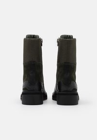 Botas de tobillo de ante verde y tela con detalles en cuero negro, que cuentan con un cierre de cremallera en la parte posterior y una suela de goma texturizada.