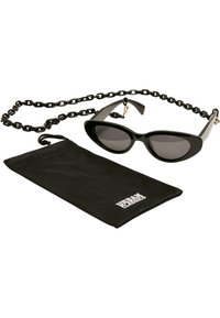 Occhiali da sole neri a forma di occhio di gatto con lenti scure, abbinati a una borsa nera testurizzata. Include una tracolla coordinata con catene.