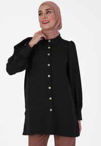 Black button-up shirt with a collar, long sleeves, and puffed shoulders. Features gold-tone buttons and a relaxed fit. Soft texture.