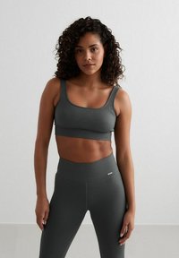 Grijze geribde sportbeha met verstelbare bandjes en bijpassende high-waisted leggings, met een gladde textuur en een subtiele logo-accent.}}