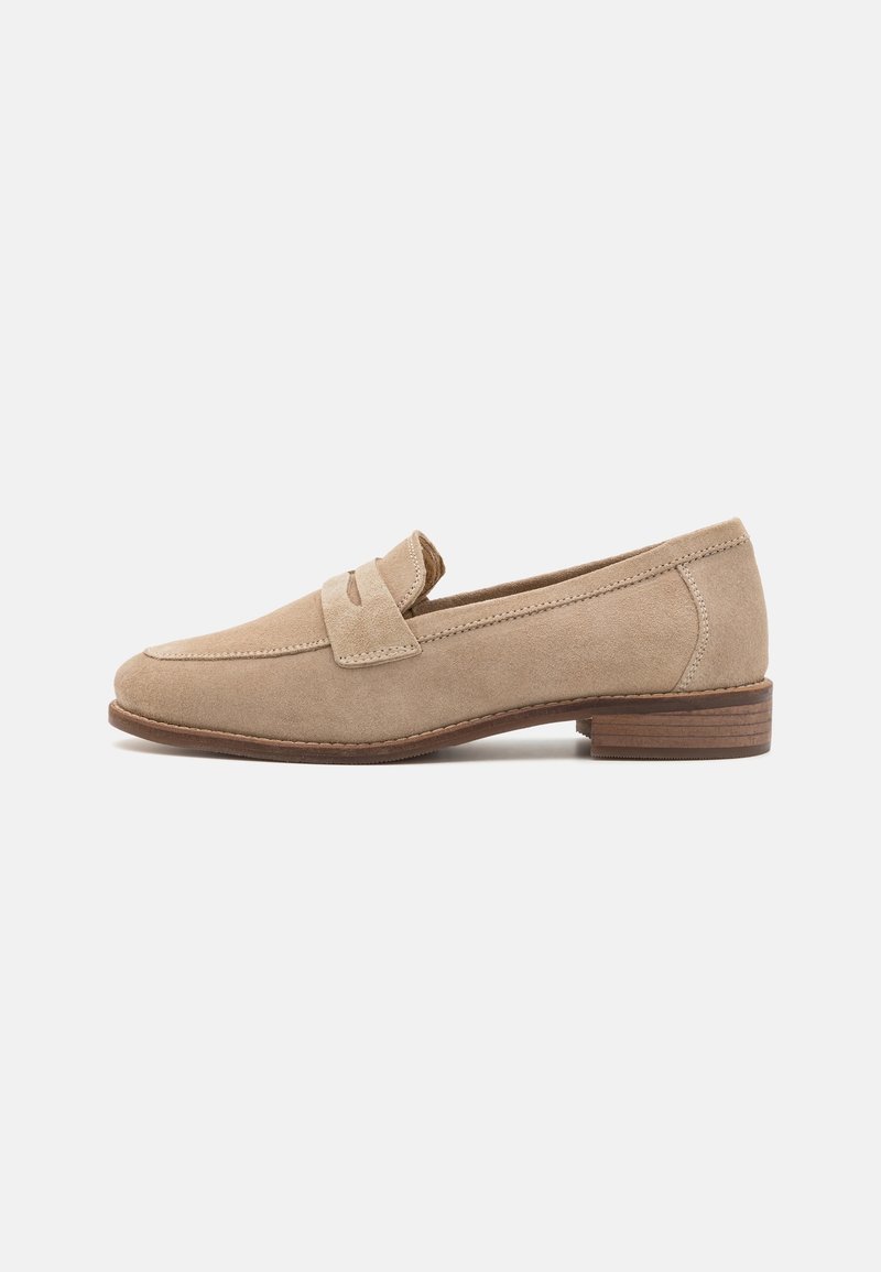 Mocassins en daim beige avec un bout rond, présentant une sangle décorative sur le devant et un petit talon en bois empilé.