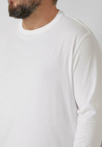 Langärmeliges weißes Baumwoll-T-Shirt mit rundem Ausschnitt, glatter Textur und lockerer Passform. Minimalistisches Design ohne Muster.