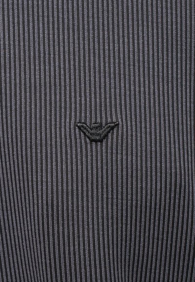 Svart stripete stoff med vertikale linjer og en liten brodert logo på venstre side. Glatt tekstur, subtil glans.