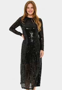 Rochie lungă cu mâneci lungi, din paiete negre, cu o siluetă ajustată, lungime medie a hămului și o textură netedă, lucioasă, care reflectă lumina.