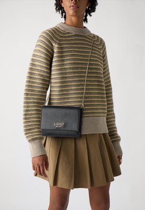 Borsa a tracolla nera in pelle con finitura testurizzata e logo dorato "LIU JO MILANO", abbinata a un maglione a righe e a una gonna plissettata.