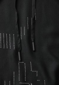 Tissu noir texturé avec un motif à clous en argent. Présente des cordons de serrage noirs avec des embouts noirs. Le design inclut des motifs de lignes et de points.