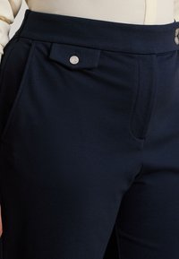 Námornícke modré nohavice vyrobené z hladkého materiálu s širokým pásom, s bezpečným zapínaním na gombík a bočnými vreckami.