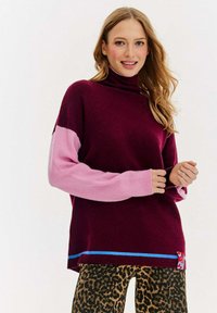Burgundowa sweter z golfem, z różowymi rękawami, niebieskim dołem i spodniami w panterkę. Miękka tekstura z odważnym wzorem bloków kolorystycznych i detalami.