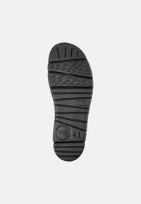 Suola di scarpa in gomma nera con motivi testurizzati a onde e linee, logo impressa e indicazioni di taglia su un accento rotondo.