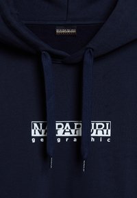 Sudadera de color azul marino con una textura suave, que presenta un logo gráfico blanco, capucha con cordón y puños acanalados. Sin patrones ni acentos visibles.