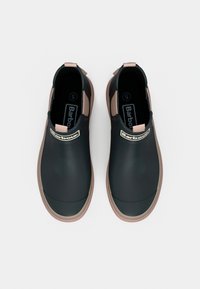 Μαύρα γκέτα από καουτσούκ με γυαλιστερό φινίρισμα, ανοιχτό καφέ λεπτομέρειες, ταινίες έλξης και λογότυπο στο πλάι. Ομαλή υφή με στρογγυλεμένη μύτη.