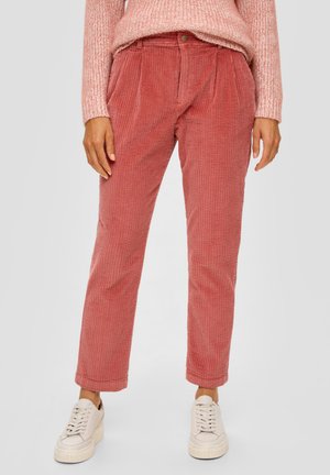 Mujer vistiendo pantalones de pana color rosa polvoriento de talle alto con pliegues, combinados con un suéter de punto rosa claro y zapatillas blancas con plataforma.