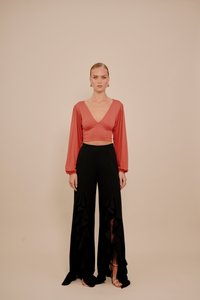 Rode cropped top met lange mouwen en een V-hals, gecombineerd met zwarte, hooggetailleerde broek met ruches en zijopeningen. Zilveren sandalen met bandjes.