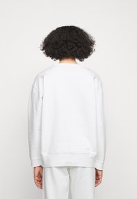 Valkoinen huppari, jossa on rento istuvuus, pyöreä kaula-aukko ja ribbaus hihansuissa. Valmistettu pehmeästä kankaasta, jossa on sileä pinta ja minimaalinen yksityiskohtaisuus.