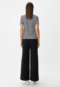 Striped black and white T-shirt paired with wide-leg black pants. The outfit features a relaxed fit and smooth fabric texture.