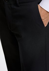 Zwarte op maat gemaakte broek met een gladde textuur, zijzakken en een klassieke snit die een strakke, moderne silhouet benadrukt.