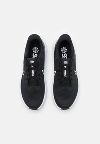 Un paio di scarpe da ginnastica nere con suole bianche e logo, tomaia in tessuto a rete e lacci, viste dall'alto su uno sfondo uniforme.