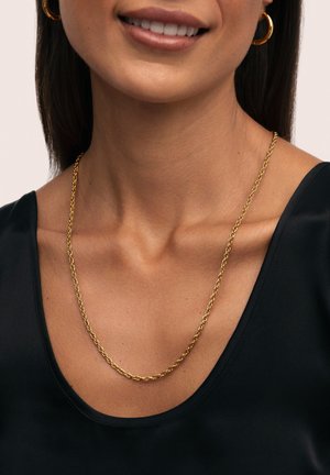 Collana a catena torciata in tono oro su un collo con tessuto nero liscio. Presenta un design delicato e intrecciato con una finitura lucida.