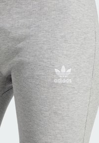 Sive rebraste tajice od mekanog materijala, sa malim bijelim Adidas logom blizu struka za brendiranje.