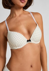 Weißer wattierter BH mit schwarzen Punkten, mit dünnen Trägern und einer kleinen schwarzen Schleife in der Mitte zwischen den Körbchen.
