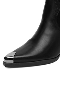 Czarne skórzane botki za kostkę z wyostrzonym czubkiem i błyszczących srebrnym czubkiem, charakteryzujące się gładką teksturą i minimalistycznym designem.