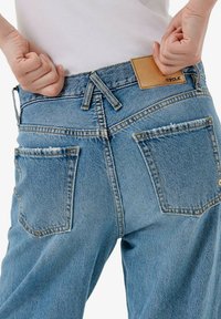 Jeans azzurri chiaro a vita alta con vestibilità rilassata. Presentano bordi delle tasche sfrangiati, una targhetta in pelle del marchio e dettagli di cuciture visibili.