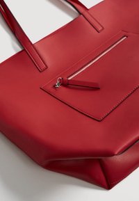 Bolso tote de cuero rojo con dos asas y un bolsillo exterior con cremallera en el panel frontal.