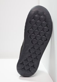 Semelle de chaussure de sport noire présentant un motif de semelle hexagonal pour une meilleure adhérence. Le matériau semble caoutchouteux avec une surface solide et texturée.