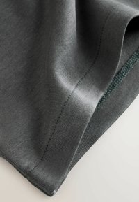 Tessuto grigio con una texture liscia e una maglia fine, caratterizzato da una leggera lucentezza e cuciture verdi lungo il bordo.