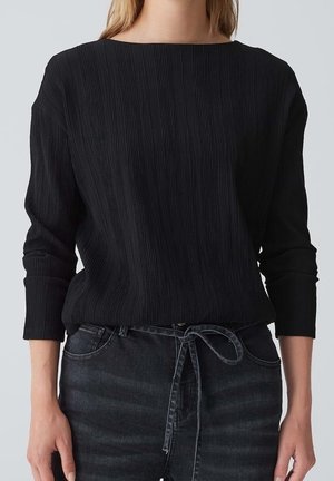 Top de manga larga texturizado negro con escote barco, fabricado en tejido acanalado y ajuste holgado, combinado con vaqueros oscuros de mezclilla.