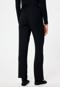 Zwarte ribbroek met een uitlopende vorm en zijsplitten aan de zoom. Gemaakt van rekbaar materiaal, met een aansluitende taille en een gestructureerd ontwerp.