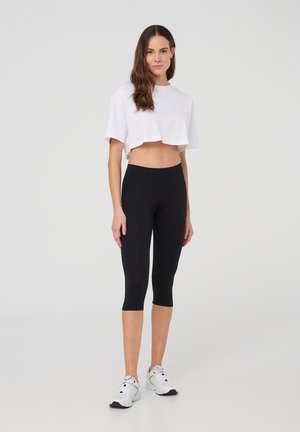 Leggings capri neri abbinati a una t-shirt corta bianca. I leggings presentano un tessuto liscio e elasticizzato, mentre la maglietta ha una vestibilità comoda.