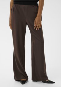 Bruine, wijde broek gemaakt van gladde stof met een elastische tailleband en zijzakken, gecombineerd met puntige zwarte hakken.
