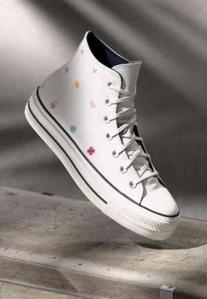 Hochschnitt-Sneaker mit weißem Canvas-Obermaterial, mehrfarbigen gestickten Designs, Gummisohle und schwarzem Streifen an der Zwischensohle.