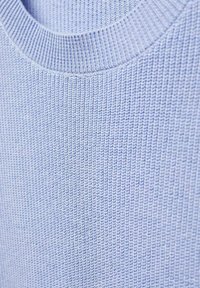 Jasnoniebieska dzianina o fakturze z pionowym prążkowaniem i okrągłym dekoltem. Miękki, elastyczny materiał widoczny na szczegółowym zbliżeniu.