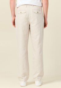 Ljusbeiga linbyxor med rak passform, två bakfickor med knappar i guldton och en slät, något texturerad yta.