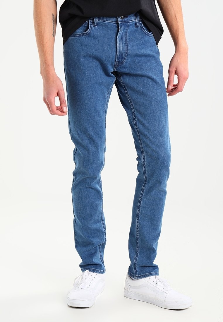 Blå denimjeans med slim fit och raka ben, med subtil blekning och kontrasterande sömmar, tillsammans med vita sneakers.