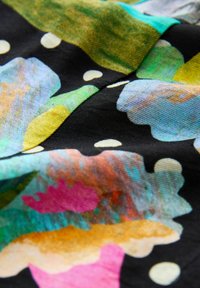 Tissu coloré présentant des motifs floraux abstraits en rose, orange, vert et bleu sur un fond noir, avec des pois blancs.