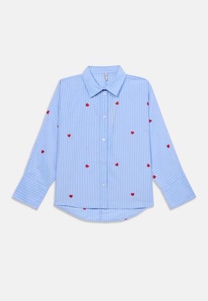 Svetlo modra srajca z belimi črtami in vezenim rdečim srcem. Ima razširjen ovratnik in dolge rokave s ukrivljenim robom.