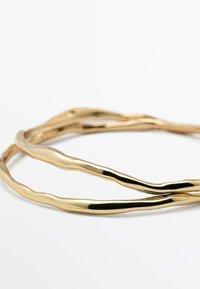 Bracciale rigido in metallo dorato con finitura liscia e lucida, caratterizzato da linee ondulate e organiche. Design regolabile e vestibilità flessibile.