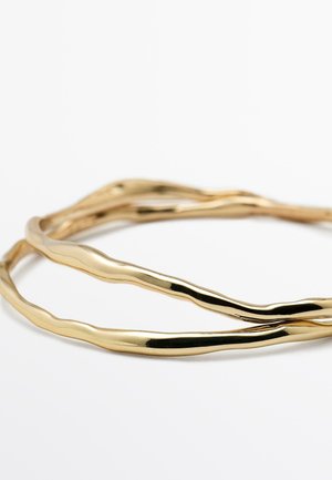 Gold-tone twisted metal bangle bracelet featuring a smooth, shiny surface with organic, wavy lines. Adjustable design and flexible fit.
