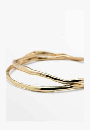 Bracciale rigido in metallo dorato con finitura liscia e lucida, caratterizzato da linee ondulate e organiche. Design regolabile e vestibilità flessibile.
