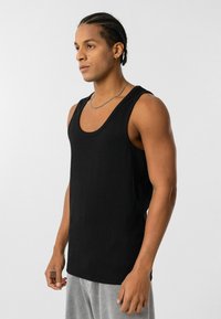 Zwarte geribbelde tanktop in een relaxte pasvorm met brede armsgaten, voorzien van een ronde halslijn en een gladde, textuurstof.