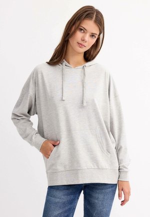 Sudadera gris con una textura suave, que cuenta con un bolsillo frontal, cordones ajustables y mangas holgadas. Llevada con jeans azules.