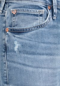 Jasnoniebieskie dżinsy z efektem zużycia. Posiadają miedziane akcesoria oraz mniejszą przednią kieszeń. Gładka faktura i klasyczny krój.