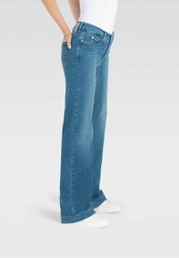 Jeans wide-leg in denim azzurro chiaro con vita media, leggera scoloritura e tasche frontali e posteriori. Abbinati a sneakers bianche.
