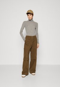 Grå turtleneck genser, brune vide cargo-bukser med brettede mansjetter, og en beige caps; glatt stoff, strukturert design, og nøytrale farger.